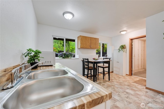 kitchen with a sink, white microwave, light countertops, and brown cabinets