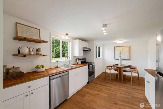 kitchen featuring butcher block countertops, stainless steel appliances, a sink, light wood-style floors, and white cabinetry