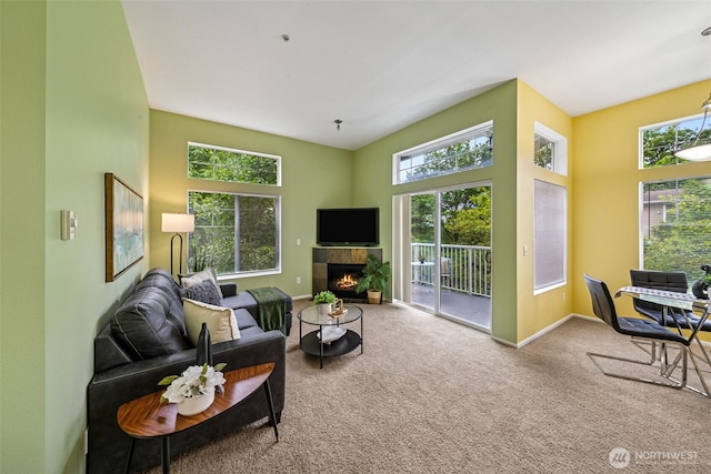 living area featuring plenty of natural light, carpet flooring, a tiled fireplace, baseboards, and a towering ceiling