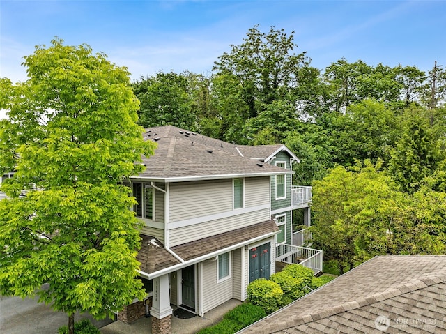view of side of home with a balcony and roof with shingles