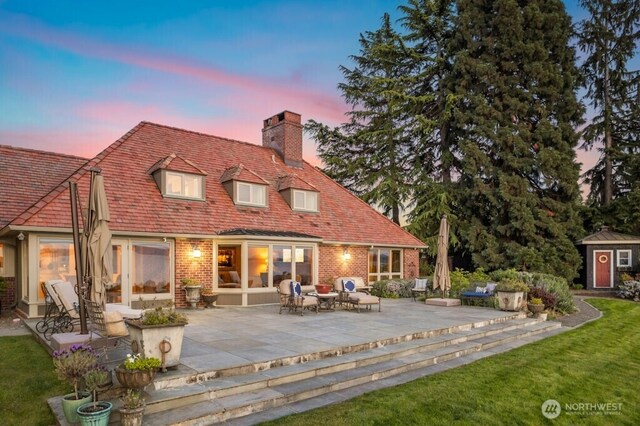 24635 8th Ave S, Des Moines, WA 98198 - back of house at dusk featuring a chimney, a patio area, brick siding, and a storage shed