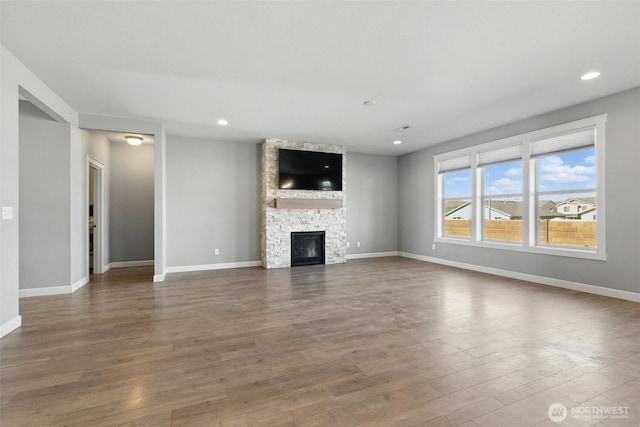 unfurnished living room featuring wood finished floors, baseboards, a stone fireplace, and recessed lighting
