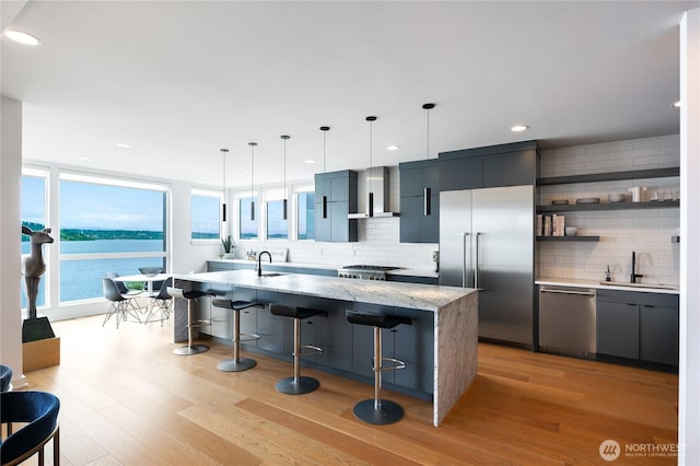 7734 Seward Park Ave S, Seattle, WA 98118 - kitchen with stainless steel appliances, a sink, wall chimney range hood, decorative backsplash, and a center island with sink