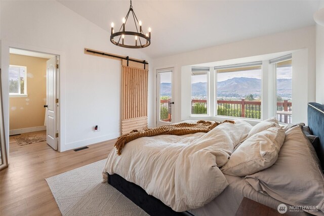 2707 Angel Ln, East Wenatchee, WA 98802 - bedroom with a chandelier, a barn door, multiple windows, light wood-type flooring, and vaulted ceiling