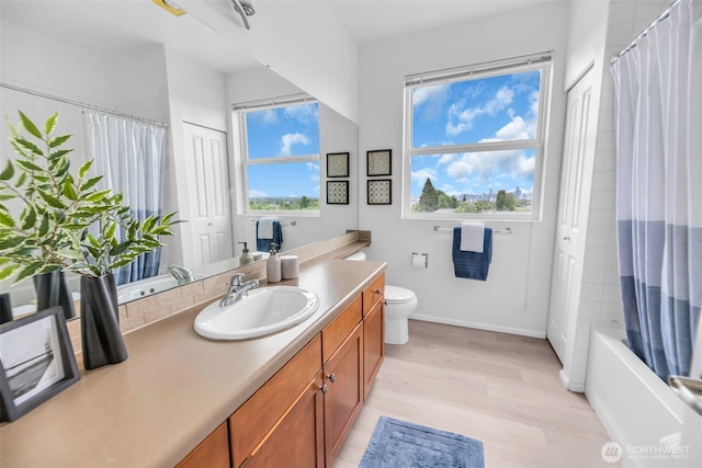 bathroom featuring vanity, wood finished floors, baseboards, toilet, and shower / bath combo with shower curtain
