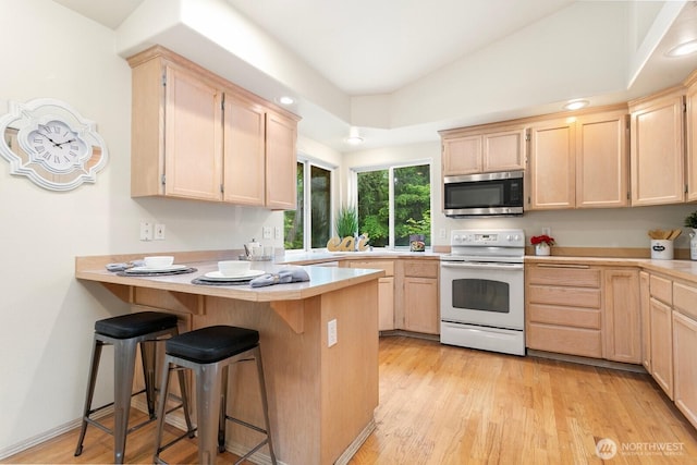 kitchen featuring stainless steel microwave, white range with electric cooktop, light brown cabinetry, a peninsula, and light countertops