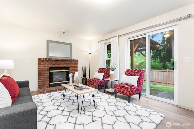 living area featuring wood finished floors, baseboards, and a brick fireplace