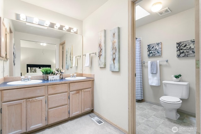 full bath with toilet, double vanity, and baseboards
