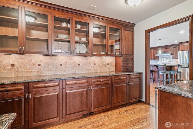 16915 32nd Ave E, Tacoma, WA 98446 - kitchen with freestanding refrigerator, under cabinet range hood, dark stone countertops, backsplash, and light wood-style flooring
