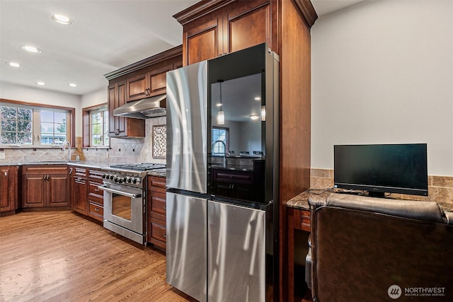 16915 32nd Ave E, Tacoma, WA 98446 - kitchen featuring appliances with stainless steel finishes, under cabinet range hood, dark stone countertops, light wood finished floors, and tasteful backsplash