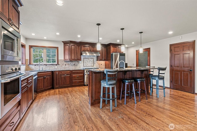 16915 32nd Ave E, Tacoma, WA 98446 - kitchen with under cabinet range hood, appliances with stainless steel finishes, a sink, light wood-type flooring, and a breakfast bar area