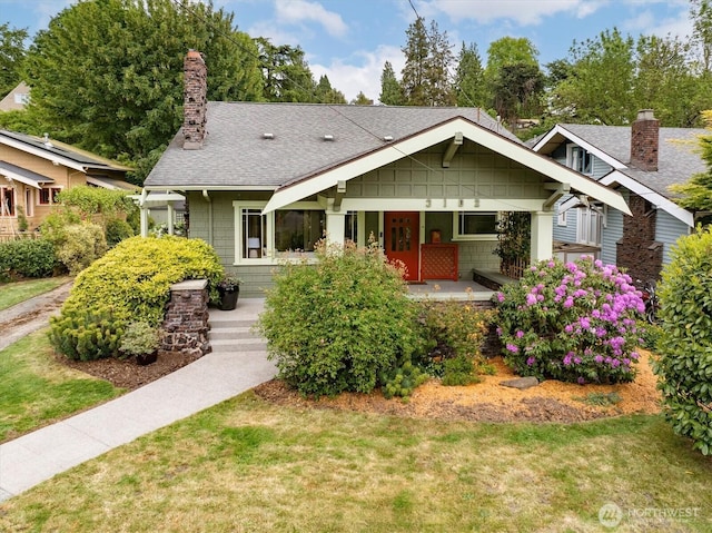 craftsman-style home featuring a chimney, a shingled roof, and a front yard
