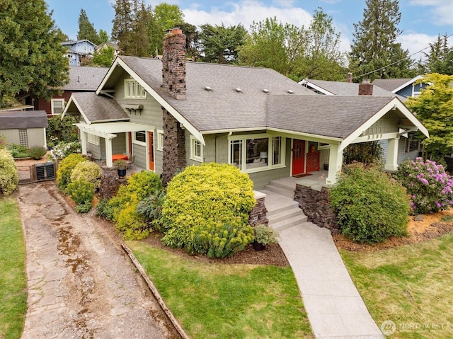 craftsman-style home featuring roof with shingles, a chimney, and covered porch