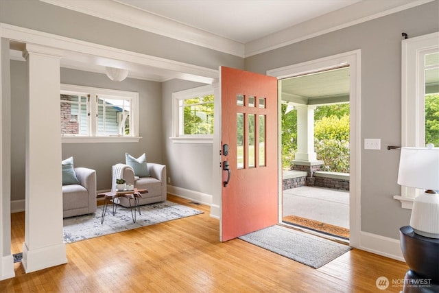 foyer with ornate columns, healthy amount of natural light, light wood-style floors, crown molding, and baseboards