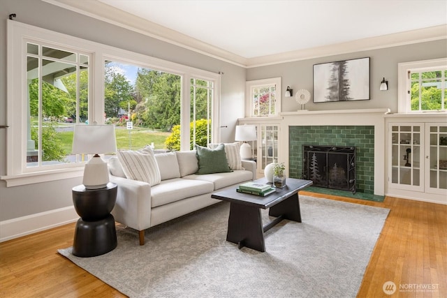 living area with wood finished floors, a fireplace with flush hearth, ornamental molding, and baseboards
