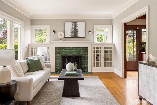 living area with wood finished floors, plenty of natural light, ornamental molding, and a tiled fireplace