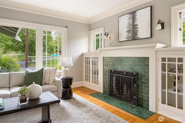 living room with wood finished floors, ornamental molding, baseboards, and a tiled fireplace