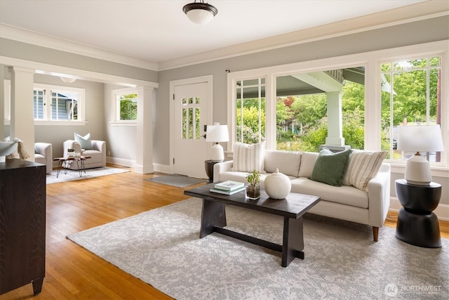 living room featuring wood finished floors, ornate columns, crown molding, and baseboards