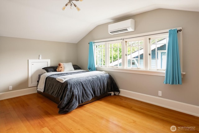 bedroom with a wall mounted air conditioner, lofted ceiling, light wood finished floors, and baseboards