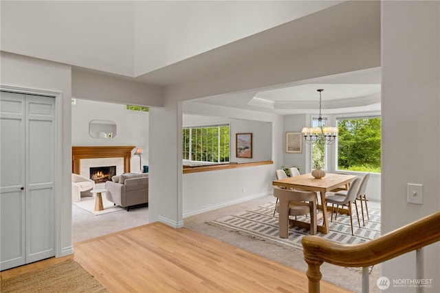 8484 NE County Park Rd, Bainbridge Island, WA 98110 - dining space with a chandelier, a lit fireplace, wood finished floors, a tray ceiling, and baseboards