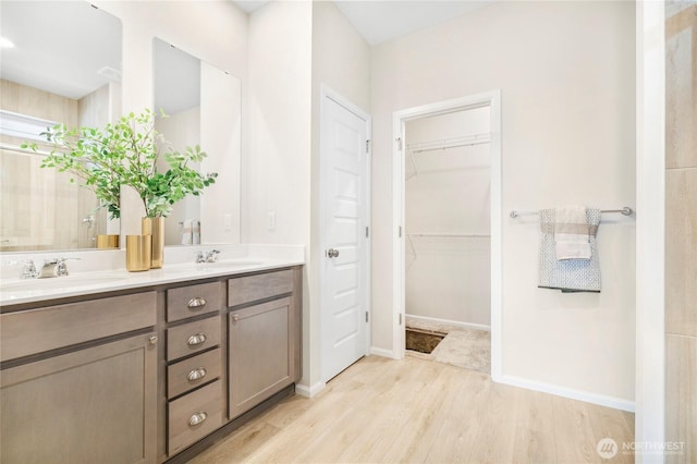 bathroom with wood finished floors, double vanity, a walk in closet, and baseboards