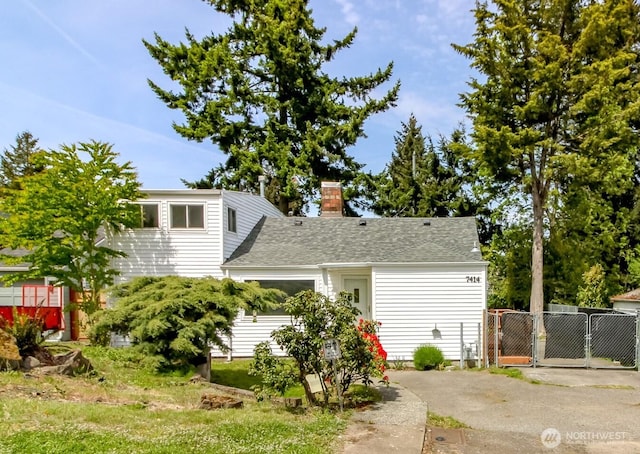 view of front of house featuring a gate, a chimney, roof with shingles, and fence
