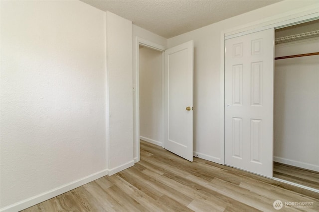 unfurnished bedroom featuring light wood-style floors, a closet, baseboards, and a textured ceiling