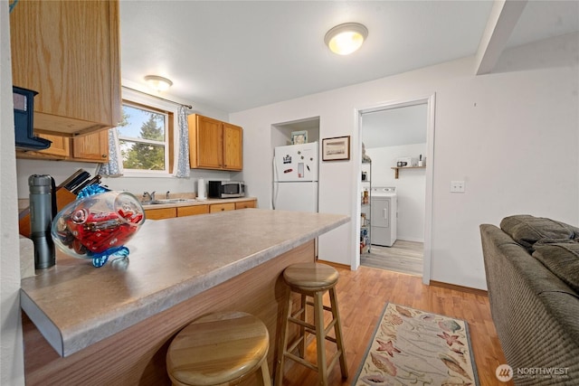 2019 Joe Johns Rd, Ocean Park, WA 98640 - kitchen featuring freestanding refrigerator, stainless steel microwave, washer / clothes dryer, a peninsula, and a kitchen bar
