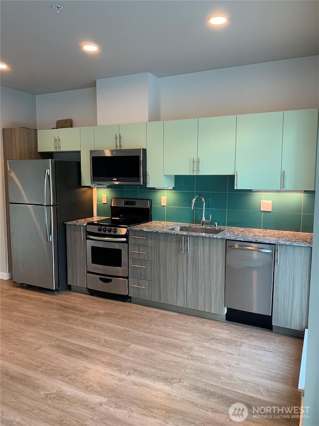 kitchen featuring appliances with stainless steel finishes, a sink, light wood-style floors, stone counters, and tasteful backsplash