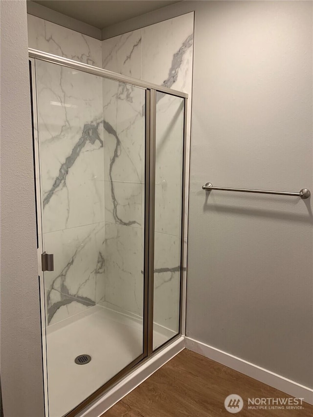 bathroom with a marble finish shower, wood finished floors, and baseboards