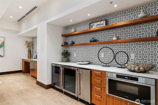 indoor bar featuring beverage cooler, baseboards, recessed lighting, backsplash, and light wood-style flooring