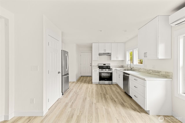 320 Kearney St, Centralia, WA 98531 - kitchen with stainless steel appliances, an AC wall unit, under cabinet range hood, light wood finished floors, and white cabinetry