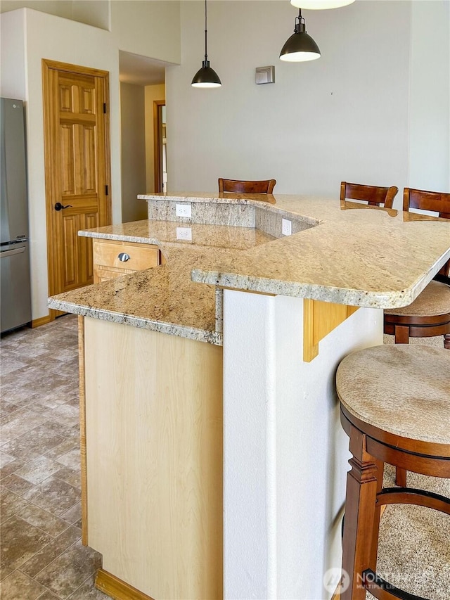 510 Oregon Ave N, Long Beach, WA 98631 - kitchen featuring freestanding refrigerator, light stone counters, a kitchen bar, pendant lighting, and a kitchen island with sink