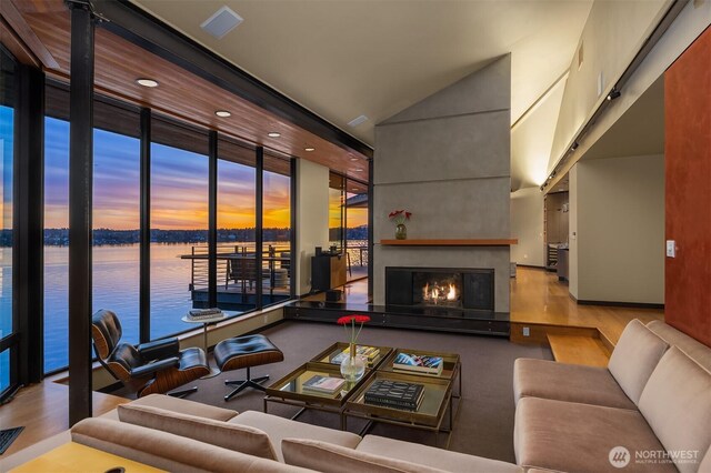 7703 W Mercer Way, Mercer Island, WA 98040 - living area featuring a water view, a lit fireplace, a towering ceiling, and wood finished floors
