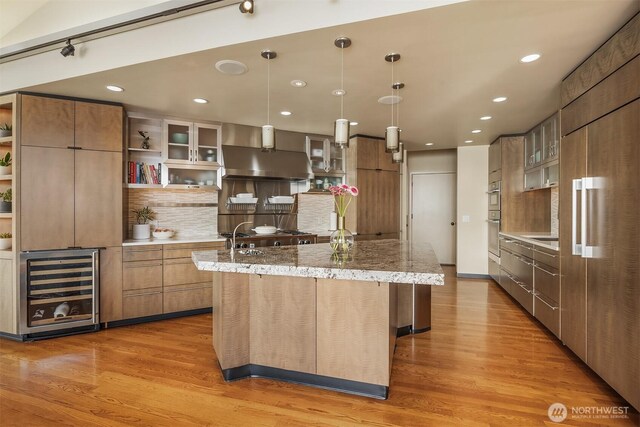 7703 W Mercer Way, Mercer Island, WA 98040 - kitchen with wine cooler, wall chimney exhaust hood, modern cabinets, open shelves, and a center island with sink