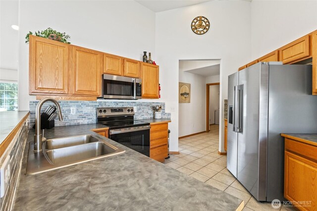 9488 SE Benjamin Way, Moses Lake, WA 98837 - kitchen with appliances with stainless steel finishes, a towering ceiling, a sink, decorative backsplash, and light tile patterned floors