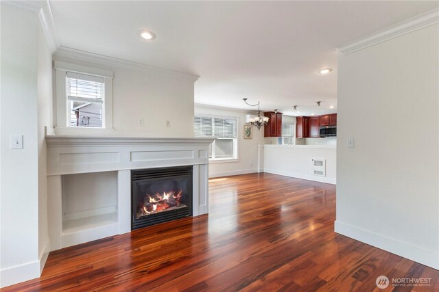 unfurnished living room with crown molding, a chandelier, healthy amount of natural light, a glass covered fireplace, and dark wood-style floors