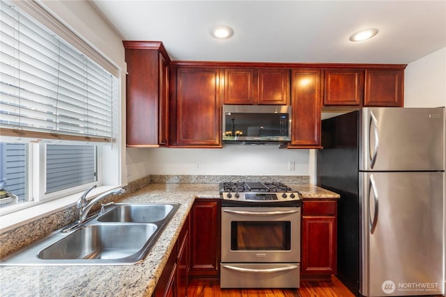 kitchen with appliances with stainless steel finishes, dark brown cabinets, a sink, dark wood-type flooring, and recessed lighting
