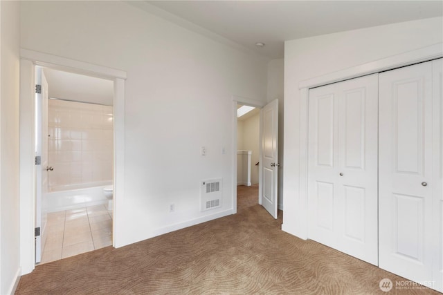 unfurnished bedroom featuring a closet, carpet floors, connected bathroom, and tile patterned flooring
