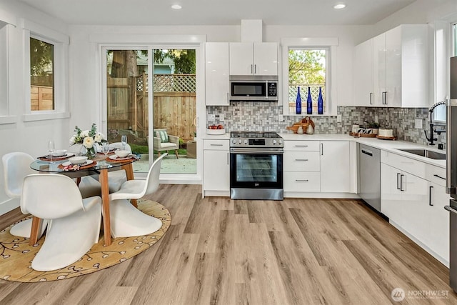 7350 21st Ave NW, Seattle, WA 98117 - kitchen featuring appliances with stainless steel finishes, light countertops, white cabinets, backsplash, and light wood finished floors