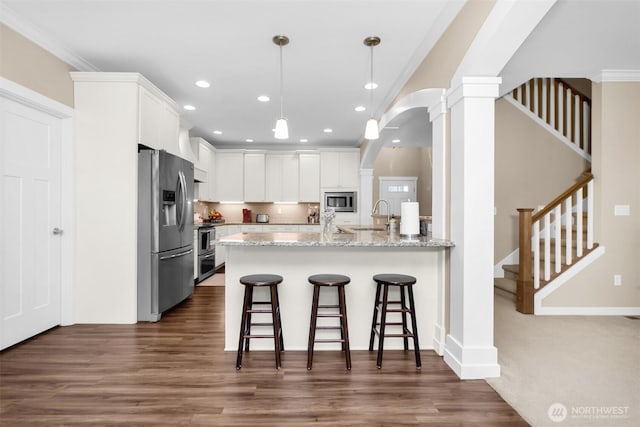 kitchen with stainless steel appliances, decorative columns, a peninsula, a kitchen breakfast bar, and white cabinets