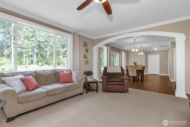living room with arched walkways, ornamental molding, a ceiling fan, a chandelier, and baseboards