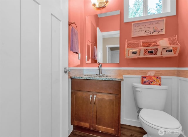 bathroom featuring toilet, vanity, wood finished floors, and a wainscoted wall