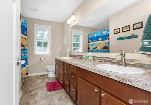 full bathroom with baseboards, healthy amount of natural light, toilet, and double vanity