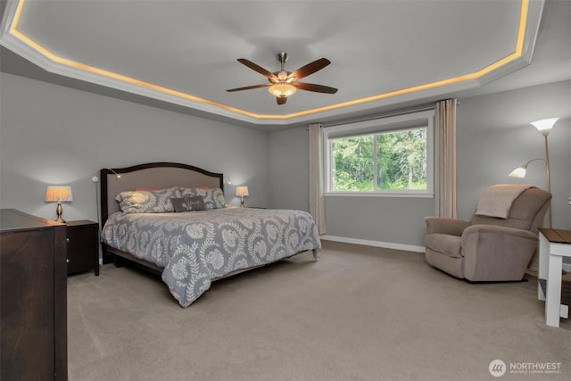 carpeted bedroom with a raised ceiling, baseboards, and a ceiling fan