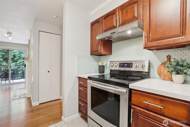 13209 Newcastle Way Unit A308, Newcastle, WA 98059 - kitchen with stainless steel electric range, under cabinet range hood, decorative backsplash, brown cabinetry, and light wood-style floors