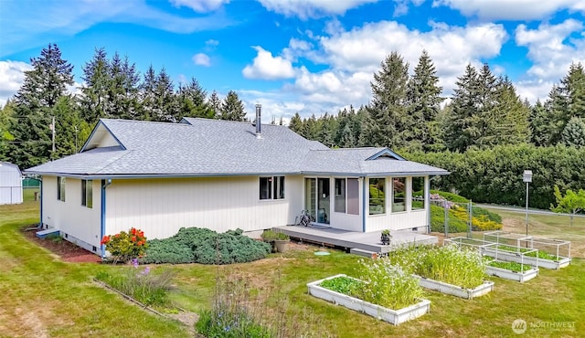 back of property with a vegetable garden, a sunroom, a shingled roof, and a yard