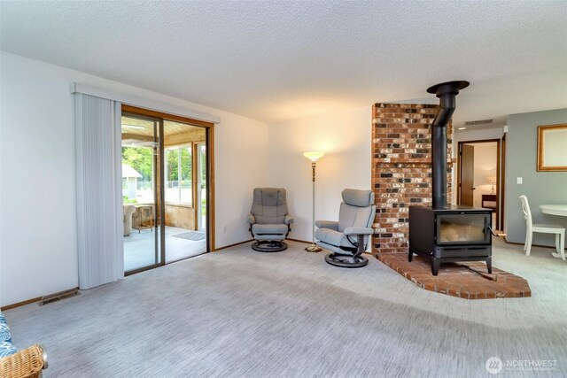 sitting room featuring a wood stove, carpet floors, and a textured ceiling