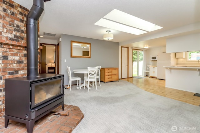 living room with a wood stove, healthy amount of natural light, a skylight, and light wood-style floors
