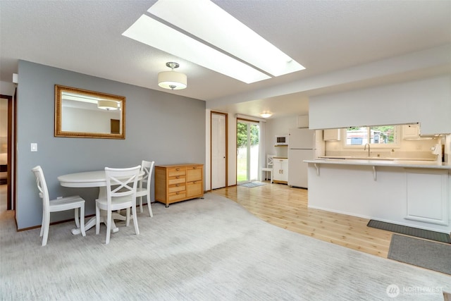 dining space with a skylight, healthy amount of natural light, and light wood-style floors